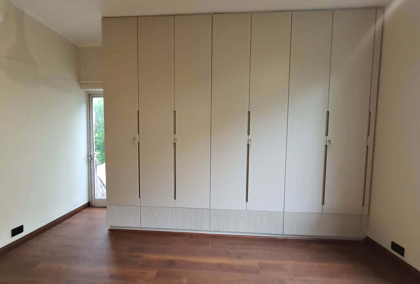 Custom floor-to-ceiling wardrobe with fluted base and groove handles in a Gurgaon home by SpaceTalk Designs